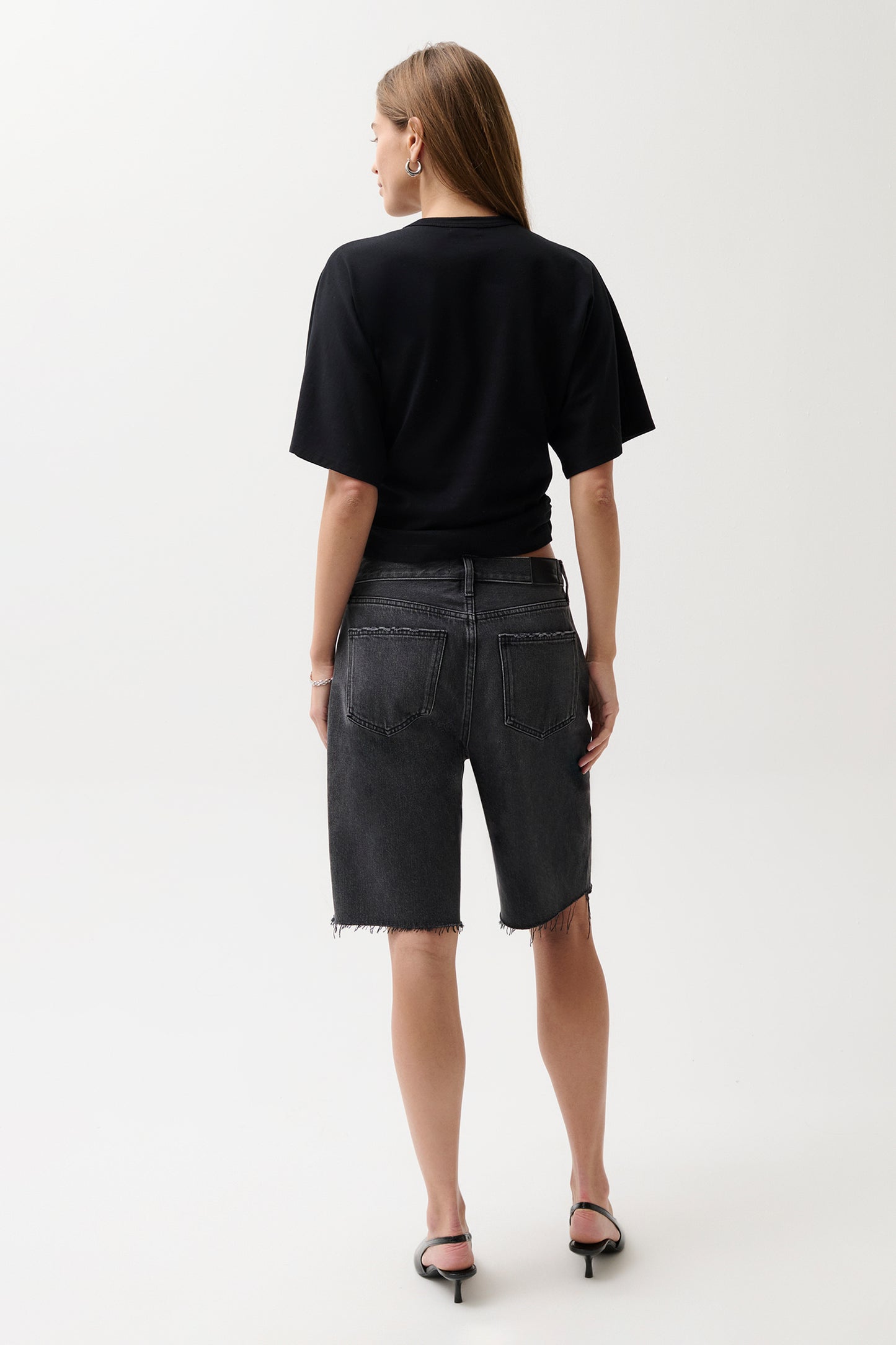 Person wearing a black t-shirt and dark denim shorts on a white background